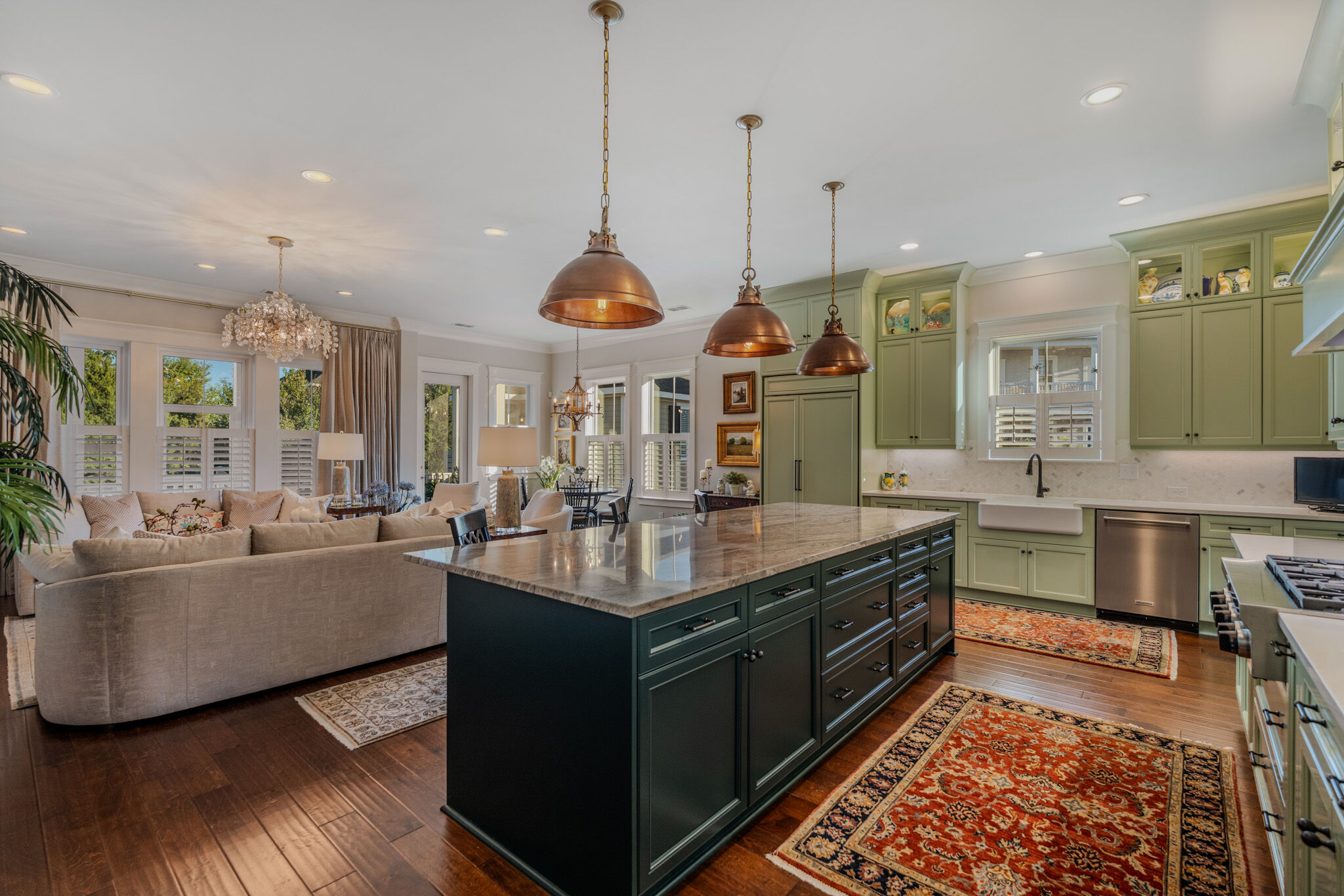 Kitchen with sage cabinetry, green island and copper pendants opening to the living room